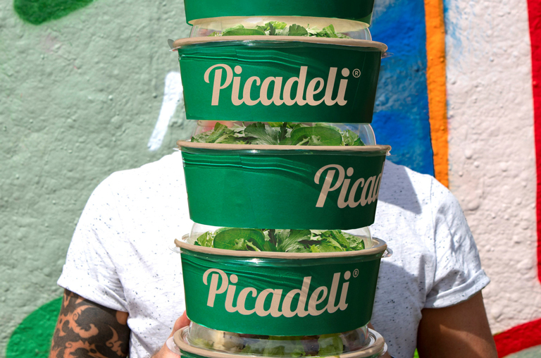 Ein Mann trägt mehrere hoch gestapelte Picadeli-Salatschüsseln