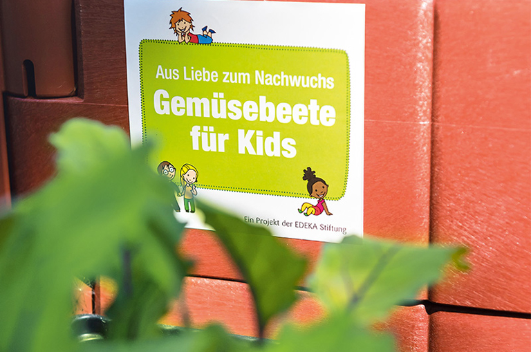 Das an einem Hochbeet befestigte Logo der Aktion "Gemüsebeete für Kids"