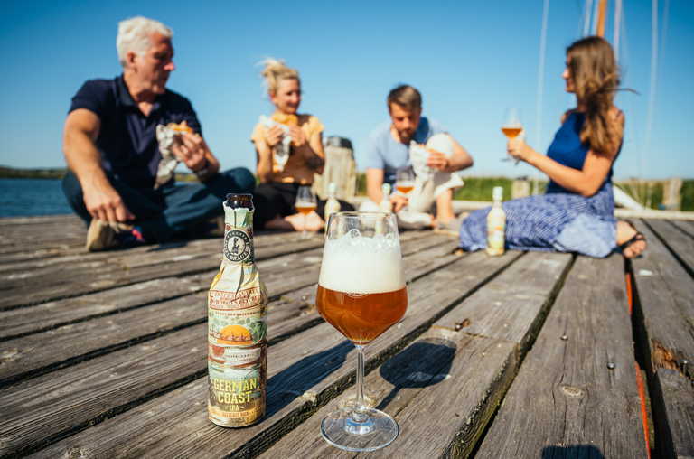 Eine Flasche German Coast Bier von der Inselbrauerei auf einem Steg auf dem Menschen das Bier genießen